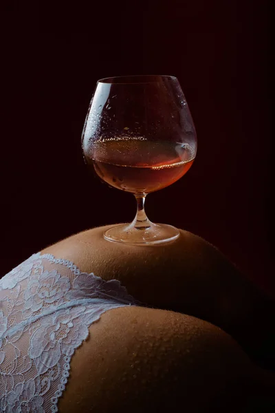 Bevanda sexy. Alcol nel bicchiere. Un bicchiere di brandy sulle natiche femminili. Mutandine lingerie e relax serale . — Foto Stock