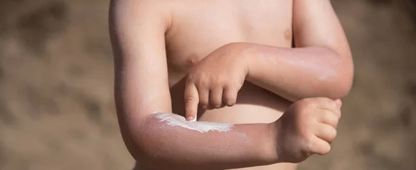 Crema bronceadora. Proteja la piel de los niños del sol en el verano. El chico se pone crema en la mano. Cuidado de la piel . —  Fotos de Stock