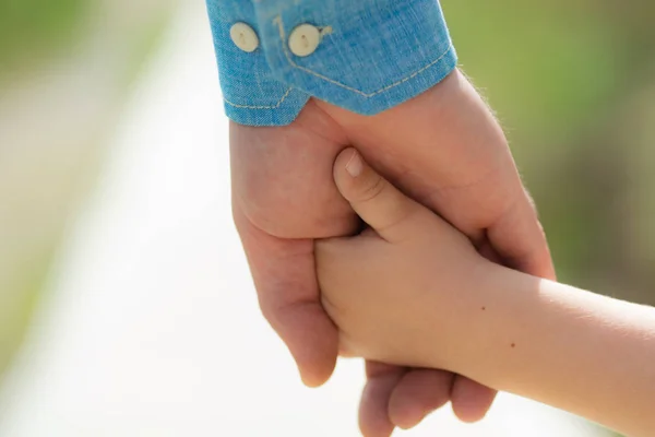 Family. Little child holding hands with his father outdoors, closeup. Family time. Closeup of two touching hands of small baby boy and male father as symbol of family love and trust. Parenthood. — Stock Photo, Image