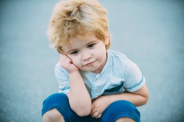 Fiú gondolkodás. Gondolkodó preschooler fiú kék út háttérben. Perc halogatás. A gyermek fáradt és guggolt. — Stock Fotó