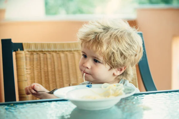 God mat, sött barn som äter spaghetti. Barnet i köket vid bordet äter pasta. Italiensk mat för barn. — Stockfoto