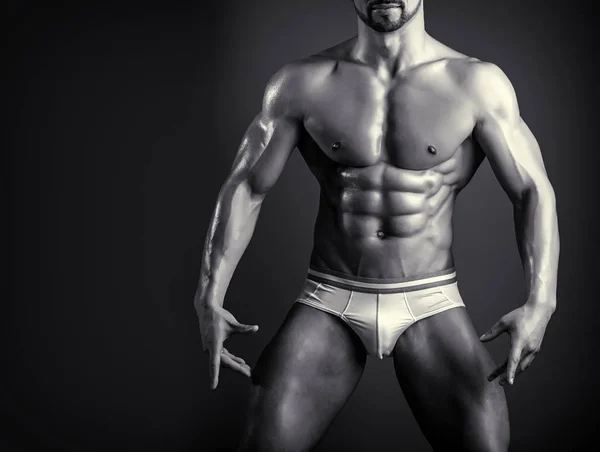 Junge Bodybuilderin zeigt Brustmuskeln, Bizeps und Sixpack-Bauchmuskeln. Schwarz-weiße Nahaufnahme des muskulösen männlichen Körpers. trainierter Mann im Fitnessstudio oder Fitnessclub. Bekleidung für Männer beim Training oder Wettkampf. — Stockfoto
