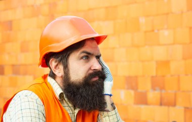 Komik inşaatçı. Kasklı bir adam hayatı düşünür. İnşaatı boz. Tuğla duvar arka plan üzerinde Üzgün sakallı işçi.