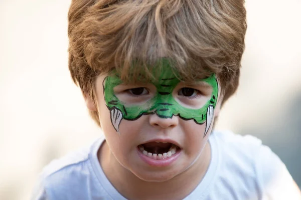 Arte corporal del dragón. Niño con una máscara en la cara. Carnaval. Héroe favorito para una fiesta infantil. Cara verde y colmillos. Un juego. Diversión para niños. Teatro de niños. Jardín de infancia y fiesta para niños en edad preescolar . — Foto de Stock