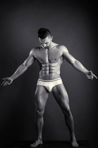 Man shows his muscules. Handsome guy in white underwear shows his well trained body. Black and white studio photo of young male model. Man looking on his abs. — Stock Photo, Image