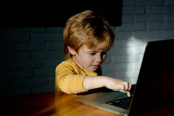 Fiú használ társadalmi hálózat telek-ra laptop otthon. Aranyos kisfiú, laptop, fehér téglafal háttérben. Ételadag-a gida-hoz megtanul számítógép tudomány. Gyerek ül az íróasztalon. — Stock Fotó