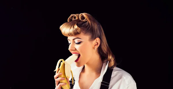 Дівчина з бананом. Молода жінка кусає банан. Вітаміни та харчування. Їжа. Дівчина їсть банан на чорному тлі ізольовано . — стокове фото