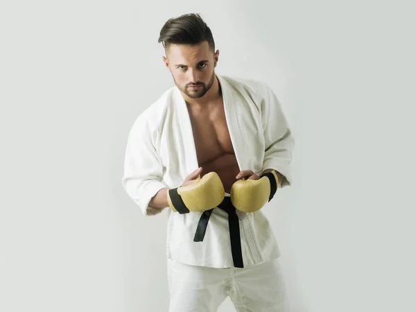 Deportista. Un tipo atractivo. Karate. Hombre en kimono con cinturón negro. El deportista usa guantes para el boxeo. El hombre hace entrenamiento de karate. Barbudo atleta con estilo antes de la pelea . — Foto de Stock