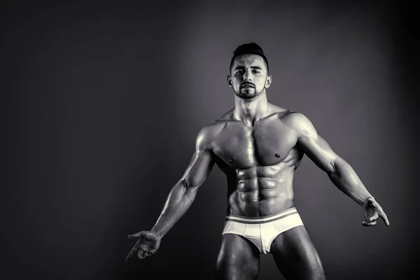 Atleta posa su sfondo scuro. Fiducioso ragazzo nudo in biancheria intima. Foto in bianco e nero elegante. Biancheria intima alla moda per uomini. Sportsman mostrando la sua tensione muscolare . — Foto Stock