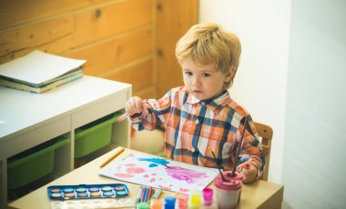 Madde. Çocuklar için sanat terapisi. Çocuk çocuk masasına parlak bir resim çizer. Sevimli genç sanatçı yaratıcılık sahiptir. Mutlu çocukluk ve duygusal sanat sınıfı. Çocuklar için yaratıcı gelişim.