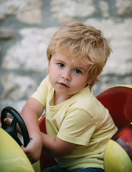 Un conductor pequeño. El niño está conduciendo un coche de juguete. Camino y viaje. Vacaciones de verano. Parque de atracciones para niños. Un chico atractivo está mirando a la cámara. Un niño pequeño aprende a conducir . — Foto de Stock