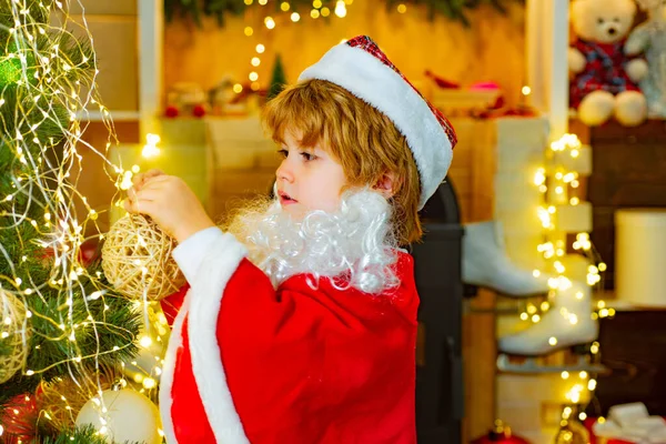 Cute boy decorates a Christmas tree. Toys for the Christmas tree. Child in santa claus costume. Christmas mood. — Stock Photo, Image