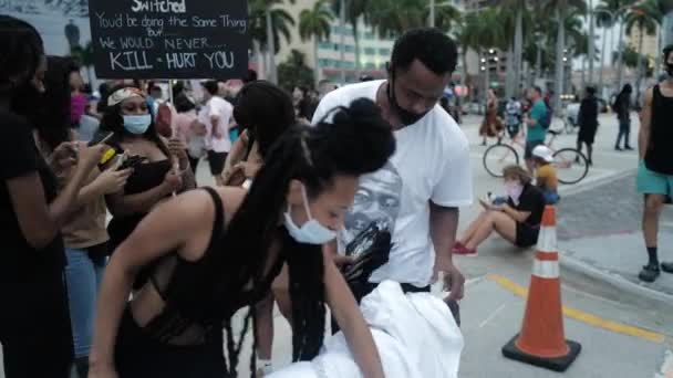 Miami Downtown, FL, ABD - 7 Haziran 2020: Irkçılığa karşı gösteriler. Siyah adam üzerinde George Floyd 'un portresi olan tişörtler satıyor.. — Stok video