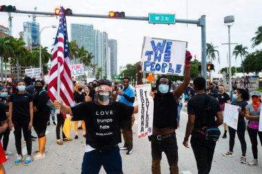 Miami, FL, ABD - 7 Haziran 2020 Love Trump tişörtlerden nefret eder. Siyah ve beyaz erkek, koronavirüs salgınıyla maskelenmiş. George Floyd 'un ölümünden sonra ABD' de düzenlenen bir gösteride posterler..