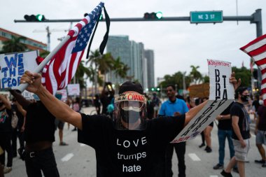 Miami, FL, USA - JUNE 7, 2020: Love Trumps hate t-shirts. White man masked by coronavirus pandemic with posters about Breonna Taylor. clipart