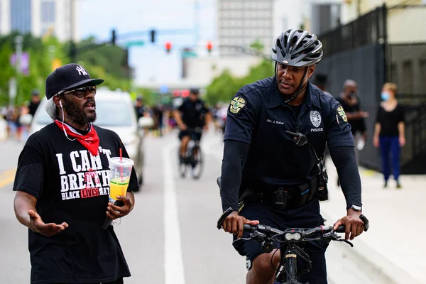 Orlando, FL, USA - JÚNIUS 19, 2020: Fekete rendőr kerékpáron és tiltakozó a rasszizmus ellen egy pólóban, olyan szöveggel, amit nem kapok meg. — Stock Fotó