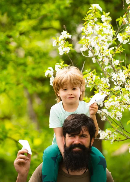 Piggyback, son sits on fathers shoulders. Happy Fathers Day concept. Family holiday. Father and son together. Daddy and son smiling outdoor on green spring background.