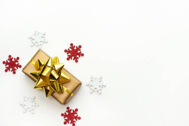Beyaz arka planda altın kurdeleli Noel hediyesi kutusu ve parlak kar taneleri. Düz yatıyordu. Kopyalama alanı