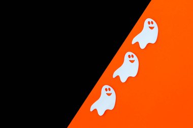 Siyah-turuncu arka planda şirin beyaz hayaletler. Mutlu Cadılar Bayramı, yaratıcı tebrik kartı. Üst görünüm, düz görünüm, kopyalama alanı