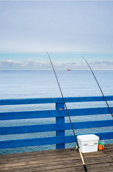 Two fishing rods leaning against the wooden rail of a pier on the Baltic Sea. Fishing at sea.