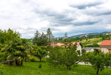 Eski küçük kasabanın caddesi bulutlu mavi gökyüzüne karşı yeşillik içinde boğuluyor.