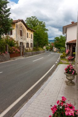 Eski küçük kasabanın caddesi bulutlu mavi gökyüzüne karşı yeşillik içinde boğuluyor.