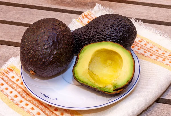 Avocados lie on an embroidered towel on a wooden table