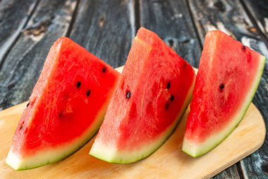 Üç dilim olgun kırmızı karpuz kesme tahtasının üzerinde bulunur. Yakın plan..