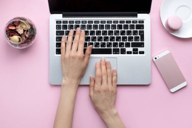 Genç bir kadın pembe arka planda dizüstü bilgisayarda yazıyor. Serbest çalışma, blog yazma ve uzaktan çalışma kavramı