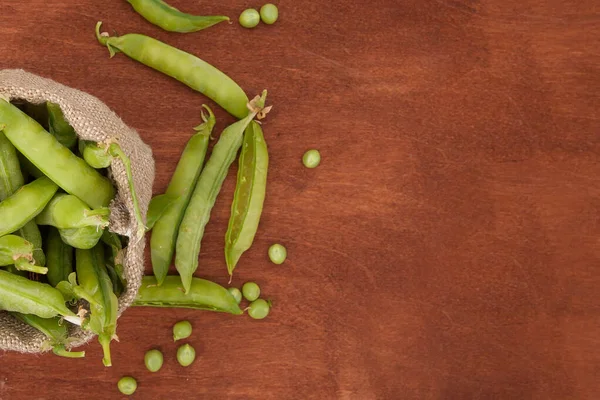 green peas, pods and peas in a canvas bag on a wooden background. flatlay.