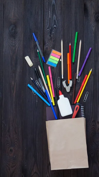 school background, school supplies, writing tools in a Kraft bag on a dark wooden background