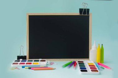 Okula, mavi arka planda kırtasiye malzemesi olan bir karatahtaya. Kopyalama alanı