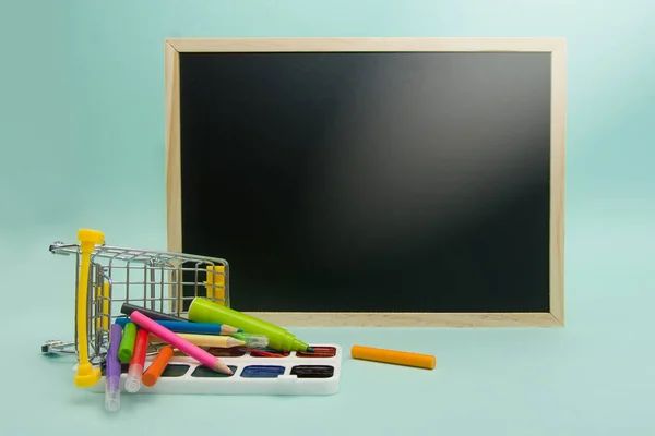 De volta à escola. Educação, venda, material de escritório em um carrinho de supermercado tombado e placa da escola em um fundo azul. Espaço de cópia — Fotografia de Stock