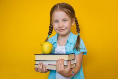 Okula dönelim. Gözlüklü, at kuyruklu güzel bir kız sarı arka planda bir yığın kitap ve sarı bir elma tutuyor. Öğrenme ve okul konsepti. Kopyalama alanı