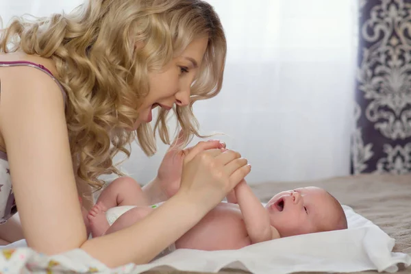 Hermosa madre rubia joven está jugando con su bebé recién nacido en la cama. Mamá y su hijo. Desarrollo temprano de una ocupación con un recién nacido. Copyspace Familia feliz y concepto . —  Fotos de Stock