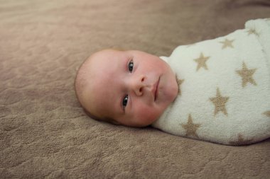 Beyaz şallı şirin bir bebek kameraya bakar ve kahverengi bir battaniyeye uzanır. 7 günlük, 1 haftalık küçük bir çocuğun güzel portresi. Kopyalama alanı