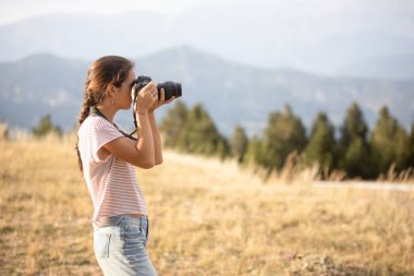 Beyaz kız gün batımında arka planda dağlarla tarlada fotoğraf çekiyor.