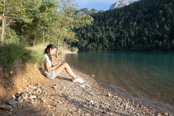 Una Chica Sonriente Sentada Junto Lago Las Montañas Usando Smartphone — Foto de Stock