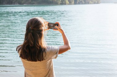 Arkadan bir kız cep telefonuyla bataklığın fotoğrafını çekiyor.