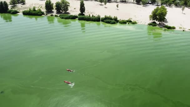 İki kişi yeşil su yüzeyindeki hüzünlü bir plaj boyunca bir kano üzerinde yüzerler. Yukarıdan bak. İHA ateşi — Stok video