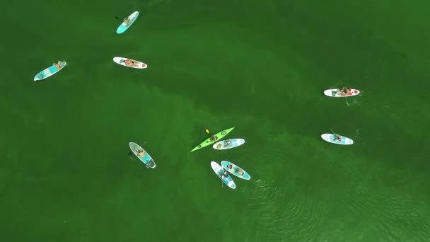 Группа гребных досок, собранных в кучу около каяка в середине зеленой поверхности воды с небольшими волнами. Вид сверху. Стрельба дронами — стоковое видео