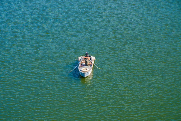 Одинокий рыбак в военной форме ловит рыбу с лодки посреди реки — стоковое фото