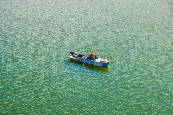 A lone fisherman in military uniform on a boat among the green water. View from above — Stock Photo, Image
