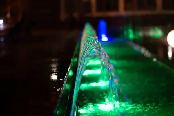 Vodní trysky s rozmazaným ostřením osvětlené v noci zelenou lucernou. — Stock fotografie