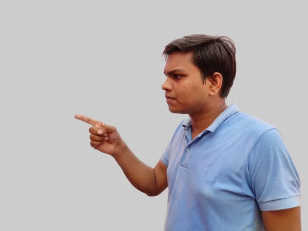 Casual dressed young Indian man in blue t-shirt pointing left with his finger in curiosity isolated on gray background — Stock Photo, Image