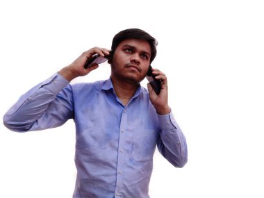 Genç adam aynı anda iki cep telefonuyla konuşuyor. Beyaz arka planda poz vermekle çok meşgul..