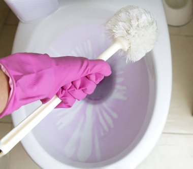 Pembe lastik eldivenli kız eli tuvalet fırçası kullanarak klozeti temizliyor. Üst taraftaki manzarada görünüyor. İyi tuvalet temizleme konsepti. Bir kadın banyo tuvaletini fırçayla temizliyor..