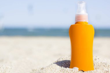 Plajda turuncu güneş kremi şişesi. Plajda güneş kremiyle yaz tatili. Deniz ve mavi gökyüzü gerçek arka plan. Mesaj için yer var. Yaz boyunca cilt koruması. Model.