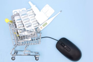 Eczanedeki alışveriş arabasında fareyle internetten mavi arka planda sipariş edilen ilaçlar. Çevrimiçi Eczane. İlaç almak için. Sağlık sigortası fikri.