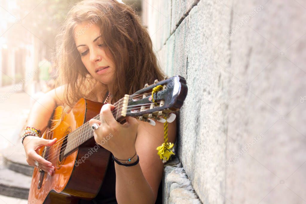 Beautiful curly brunette hair hippie girl playing guitar in the street. Freedom and free lifestyle. enjoying nature, music, life